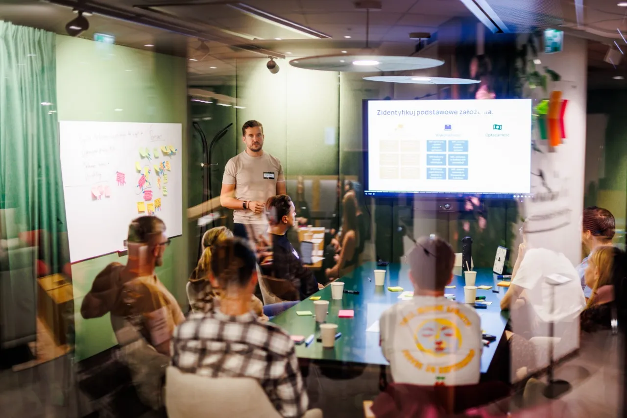 Olek running a founder workshop seen through a glass wall in 2025